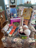 Chair displaying various knitting supplies including yarn skeins, needles, loom set, and books