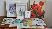 Overview of framed floral paintings, red poppy canvas, and loose watercolor and ink paintings laid out flat.