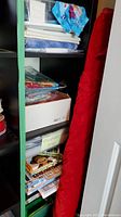 Black shelving unit holding clear plastic bins of fabric, folded fabrics on top shelf, Disney Frozen print visible, red fabric bolt leaning right.