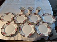 7 bread and butter plates surround 3 matching mugs on a white textured cloth, showing the full set in natural light