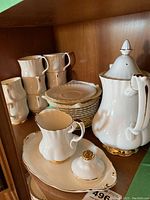 Coffee pot, creamer, sugar pot lid, serving tray, stacked saucers and cups displayed on shelf