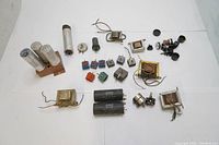 Assortment of vintage electronic components including capacitors, selenium rectifiers, transformers, and other parts laid out next to each other on a white surface.