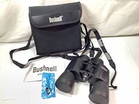 Bushnell binoculars, carrying case, instruction manual and accessories laid out on surface.