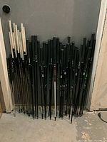 Group photo of multiple golf shafts standing upright with black and white grips against a gray wall.