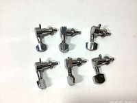Photo showing six metal guitar string tuning pegs machine heads arranged in two rows on a white background.