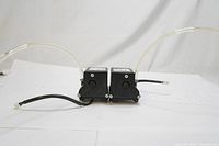 Photo of two black Thomas compressor units with attached clear tubing and electrical cables on a white background