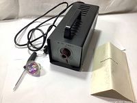 Full view of device with cable and lamp bulb next to manual booklet.