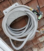 Coiled gray garden hose with brass connectors and black-green nozzle mounted on wooden siding