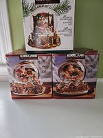 Three large Kirkland Signature musical snow globe boxes showing Christmas-themed scenes inside snow globes.