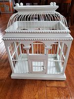 Front view of the white wooden bird cage showing decorative trim and front door closed.