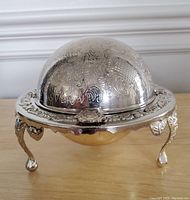 Front view of the antique silver butter dish with ornate legged base and engraved dome lid
