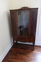Front view of antique wooden china cabinet with glass door and carved details.