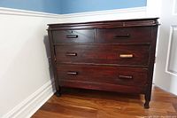 Front view of antique wooden dresser showcasing two smaller top drawers and two larger bottom drawers with wood handles, positioned in a room corner on hardwood floor.