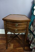 Front view of antique wooden end table showing two drawers with brass round handles and carved accents on legs.