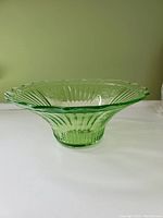 Side view of round green depression glass bowl with scalloped edges, ribbed design and textured details in good condition.