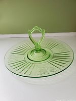 Front angled view of the green Depression glass serving dish with a center handle and etched floral and linear patterns.