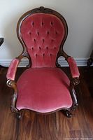 Front view showing pink velvet upholstery with button tufted backrest and carved wooden frame with armrests and cabriole front legs.