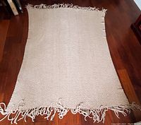 Beige throw blanket laid out flat on wood floor, showing knit texture and fringed edges