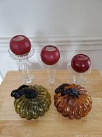 Two blown glass pumpkins and three red candles with glass holders, front view