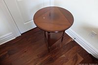 Wooden round folding Bombay side table in open position showing surface with wood grain and single leg set