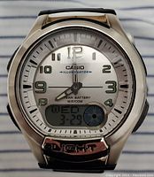 Close-up of watch face showing analog dial with numbers, luminous hands, digital display for day and date, and LIGHT button on bezel.