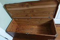 Open cedar chest showing interior wood panels, metal hinges, and stamped logo inside lid and base.