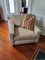 Front and slight angle view of beige upholstered Sklar Peppler chair with striped pillow in room with wooden floor.