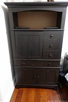 Front view of black wooden computer cabinet with closed drawers and doors