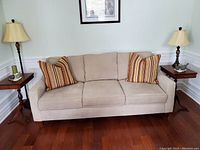 Front view of beige upholstered sofa with three seat and back cushions