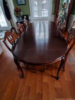 Top front view of the dark wood dining table with chairs arranged around it, showing polished surface and curved legs.