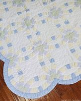 Close-up of the scalloped edge of the quilt showing the detailed patchwork rings in pastel colors and blue border.