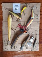 Photo showing nine used deep fishing lures of various sizes and types laid on a cardboard sheet.