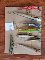 Photo showing all 8 fishing lures arranged on cardboard with hooks visible and identification card