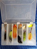 Open tackle box showing colorful fishing spinnerbaits with metal blades and feather skirts in individual compartments.