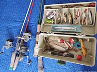 Photo showing three used fishing rods with attached spinning reels with worn handles lying on blue padding.