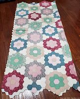 Quilt laid on hardwood floor folded lengthwise showing hexagon flower block layout