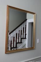 Large rectangular mirror mounted on the wall showing reflection of a staircase with white spindles and dark wood handrail.