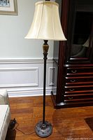 Full view of the old floor lamp showing its height, lampshade, black metal stand, and base on wood floor near furniture.