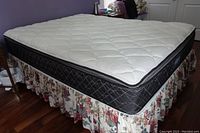 White quilted Beautyrest mattress on box spring with floral bed skirt on wooden floor