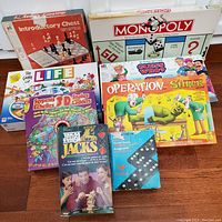 Photo showing nine assorted classic board games including Monopoly, Life, Guess Who, Operation Shrek, Introductory Chess, Serpents & Ladders, Jenga Jacks, and Dominoes.