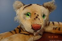 Close-up of tiger's face showing green eyes, embroidered nose, and fur texture.