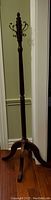 Full view of the wooden tree-style coat rack, showing the turned wooden pole, metal hooks, and four-legged wooden base on a hardwood floor.
