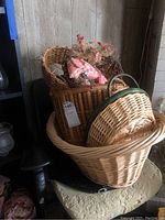 Three baskets stacked together: a large light wicker basket at bottom, a darker wood basket in the middle, and a small round wicker basket with handle and green rim on top.