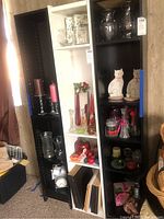 Photo showing black and white bookcase shelves filled with glass vases, candles, figurines, and other decorative items