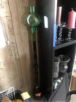 Full view of tall green glass Chianti bottle showing entire height and placement next to bookshelf
