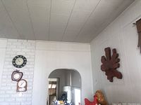 Four clocks mounted on a white brick wall and a plain wall above an interior archway. Visible clocks include a large wood wall clock, apple-shaped clock, and wire rimmed leaf clock.