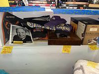 Shelf showing Baltimore Ravens autographed merchandise including caps and display case alongside assorted DVDs and VHS tapes.