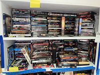 Two shelves filled with many DVD movies and boxed season sets stacked and arranged horizontally and vertically. Titles are visible showing a wide range of movies and TV shows.