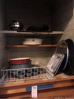 Shelf holding black electric griddle, white round bakeware, red bundt pan, muffin pans, and metal baking trays.