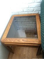 Top view of rectangular end table showing wooden frame and clear glass top reflecting white brick wall.